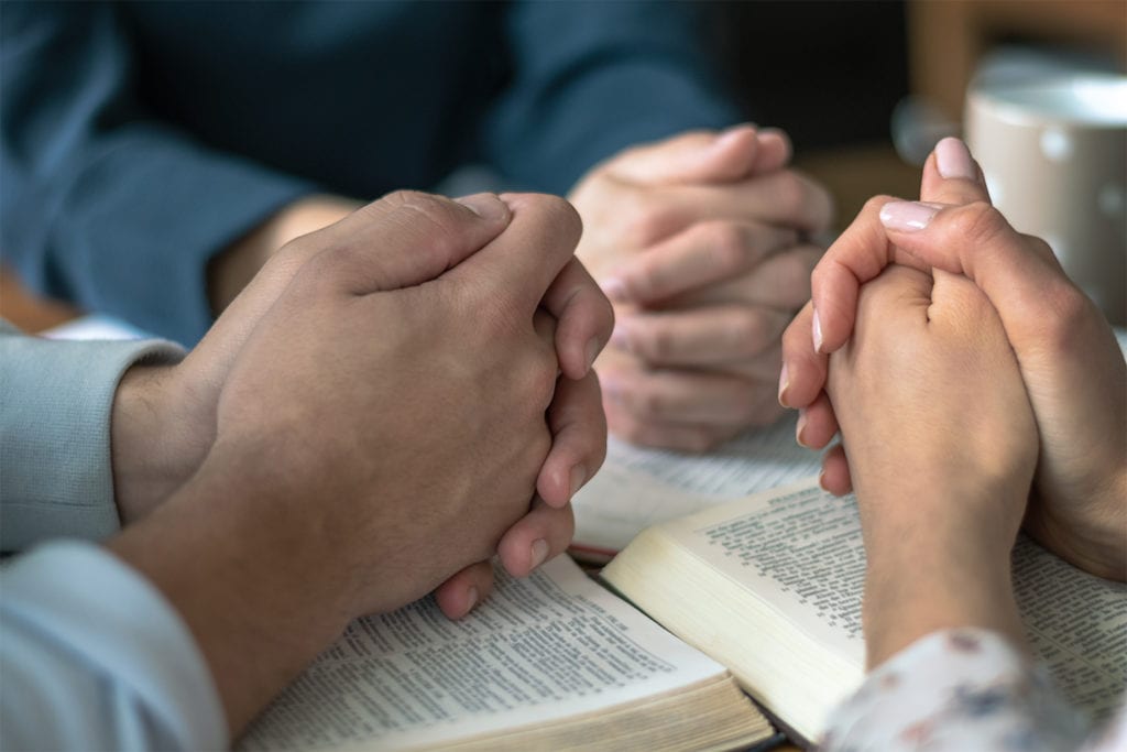 hands folded in prayer on top of Bibles at Biblestudy