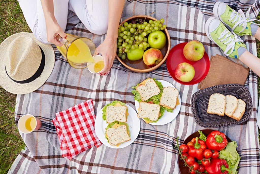 picnic food on blanket with woman pouring juice