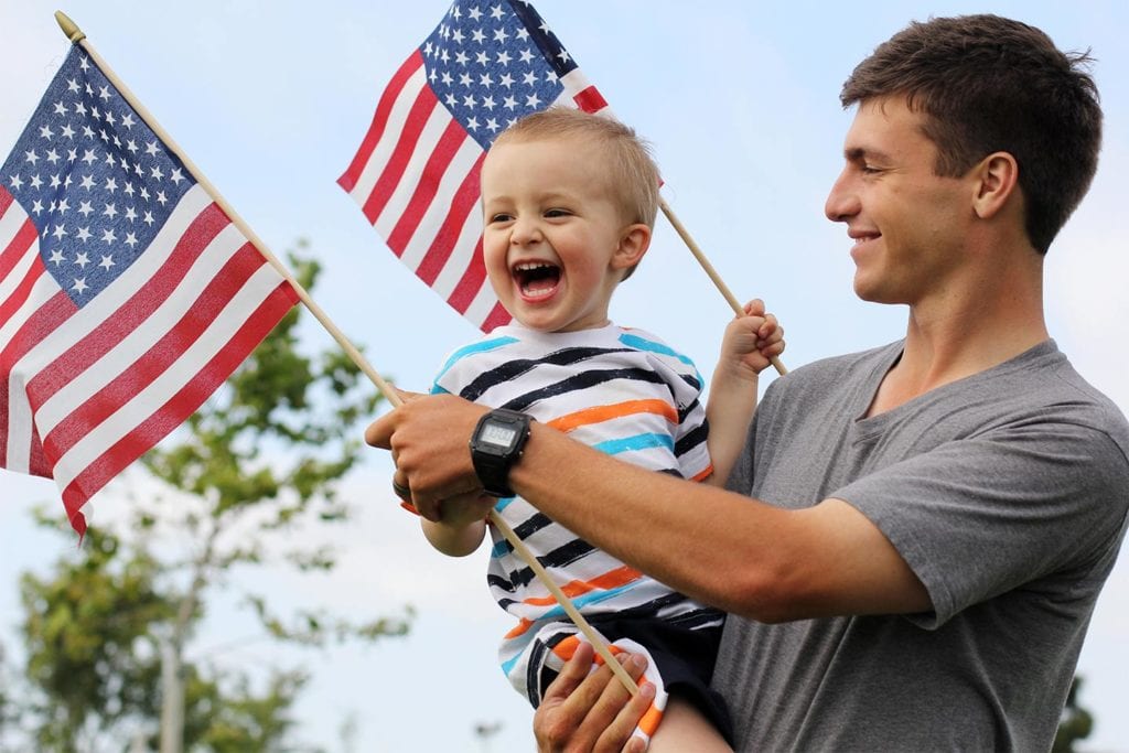 father and young son waving American flags for the fourth of July