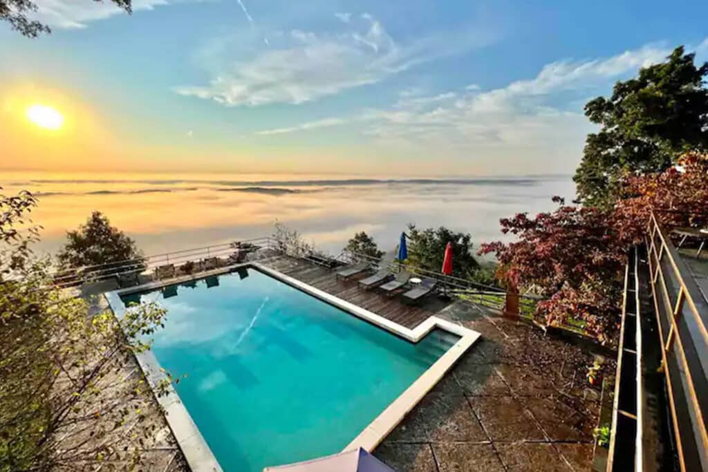 Infinity pool overlooking a serene landscape at sunset, surrounded by lush greenery and distant hills.