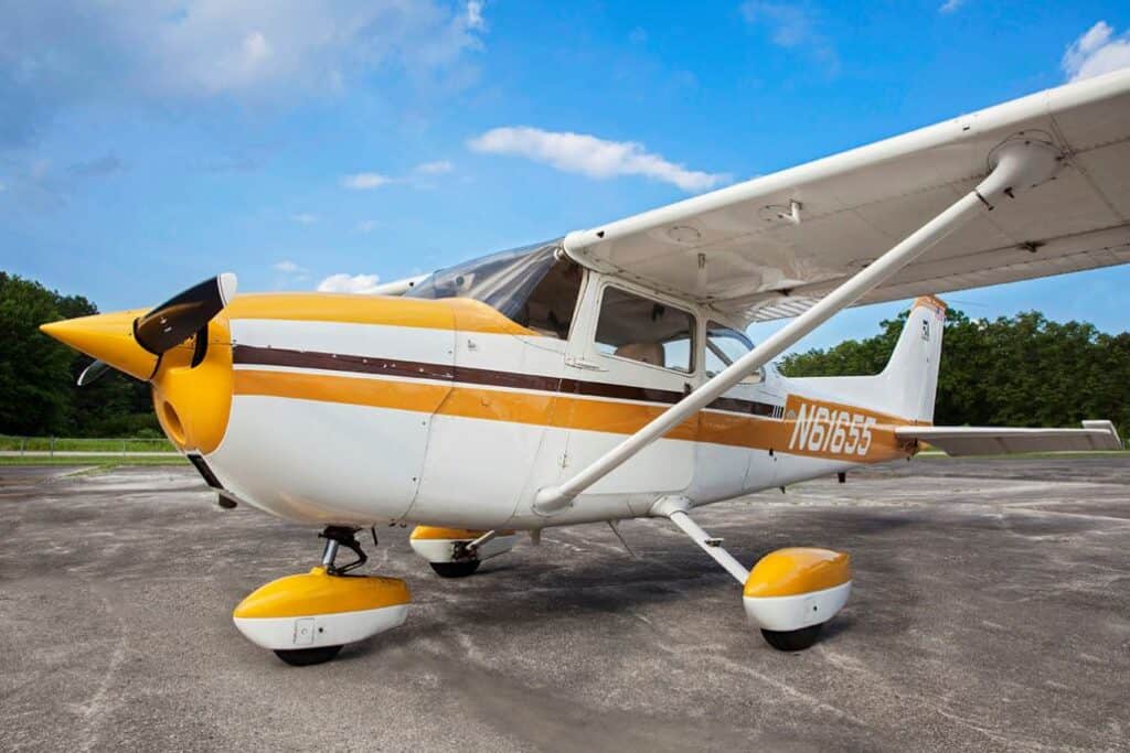 A small, vintage airplane with a white and yellow color scheme parked on a tarmac under a blue sky.