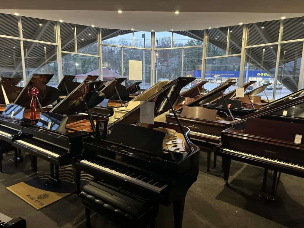 A spacious showroom filled with various grand pianos, illuminated by natural light from large windows.