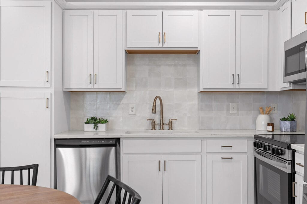 Modern kitchen featuring white cabinetry, stainless steel appliances, a sleek faucet, and minimal decorative plants.