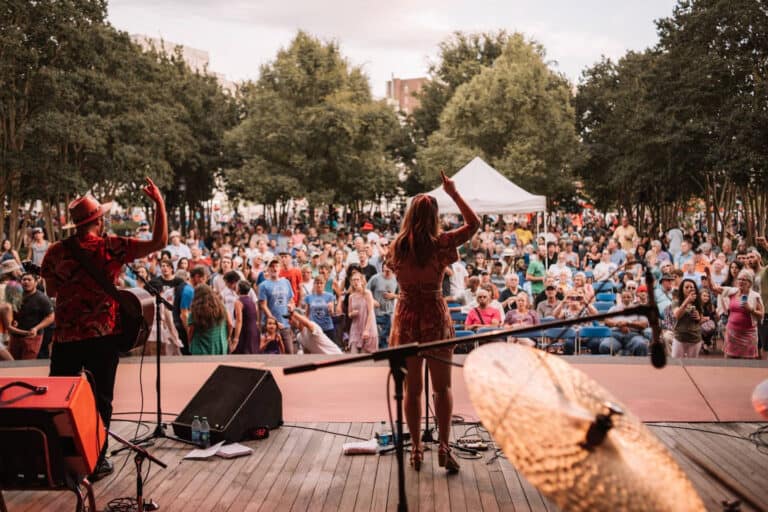 A lady on stage at a music festival with a large crowd behind her.