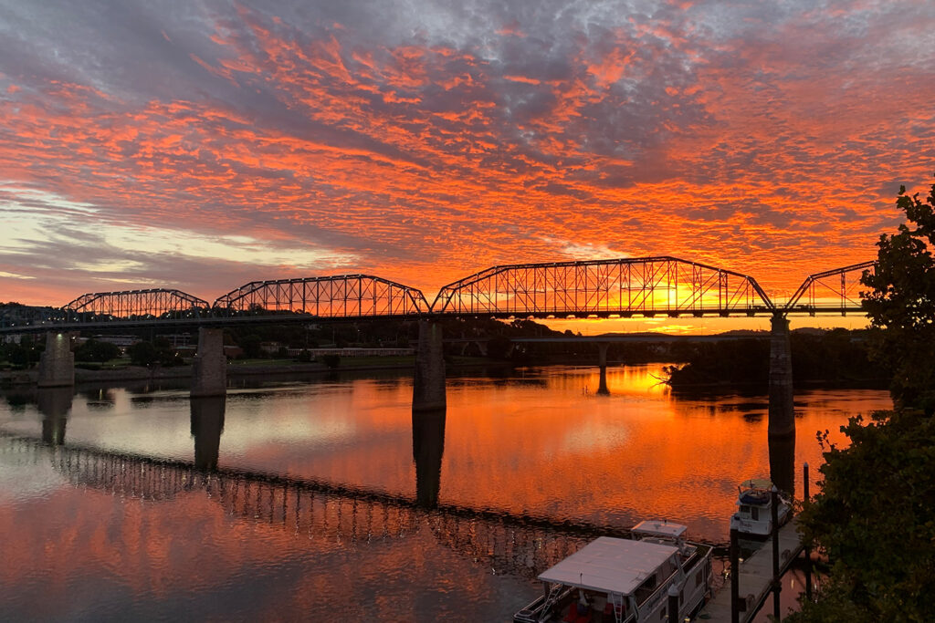 Vibrant sunset over a river with silhouetted bridge, reflecting colorful clouds and water.