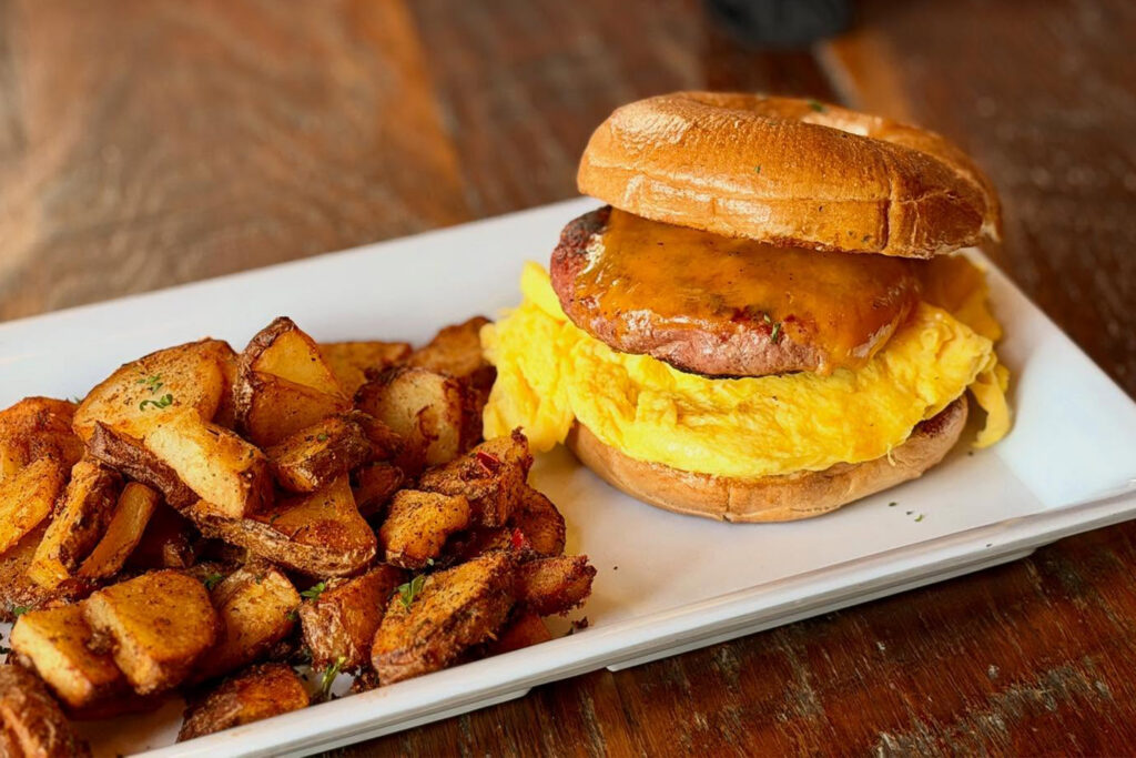 Egg and Cheese Bagel with a side of potatoes on a plate on a wooden table