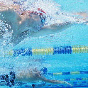 Two swimmers compete in a pool, splashing water as they race toward the finish line, showcasing intense athleticism.