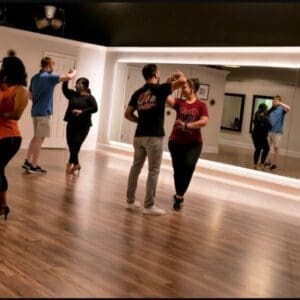 A lively dance class with couples practicing in front of a large mirror, showcasing diverse styles and movements.