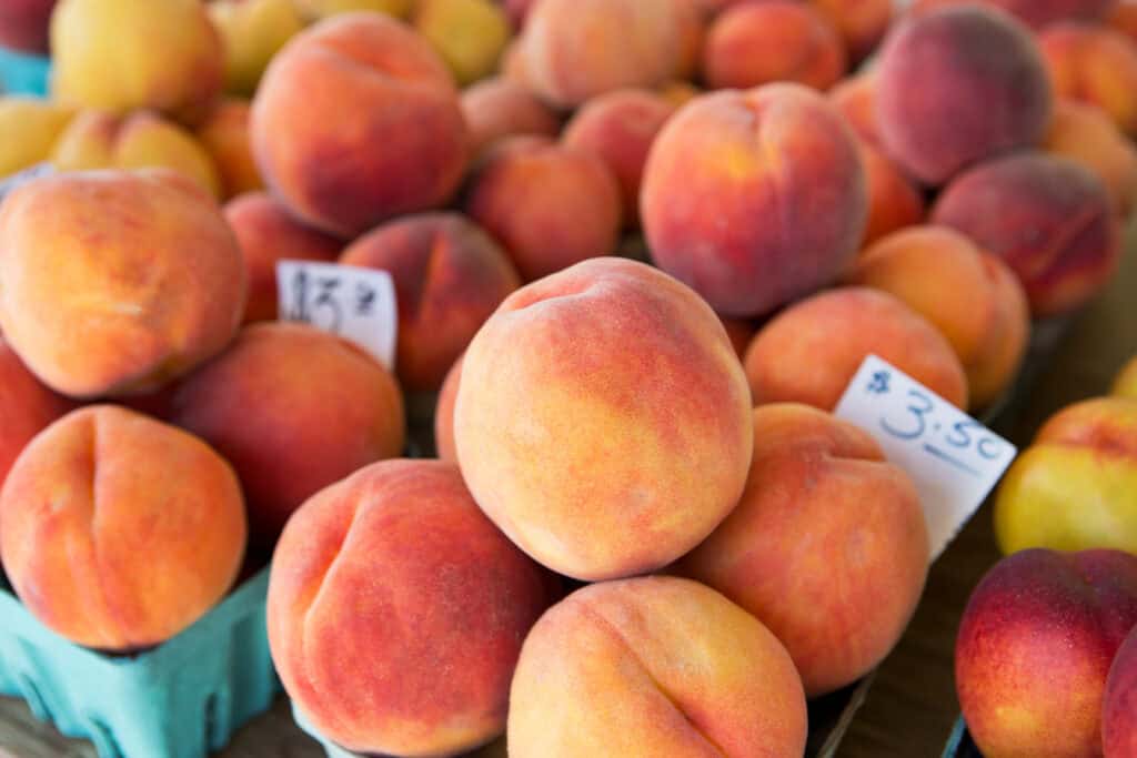 A close-up of fresh, ripe peaches in various shades of orange and yellow, displayed in blue containers with price tags.
