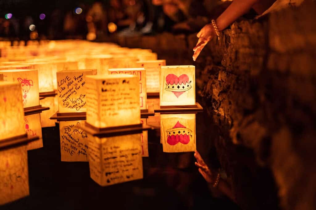 Hands placing illuminated lanterns on water, surrounded by glowing reflections, creating a serene and festive atmosphere.