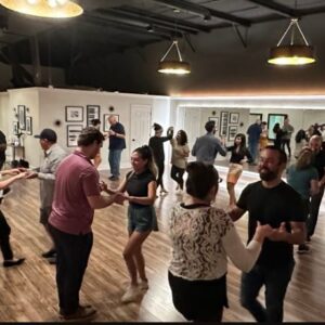 A lively dance studio with people dancing closely, mirrors on one wall, and warm lighting overhead.