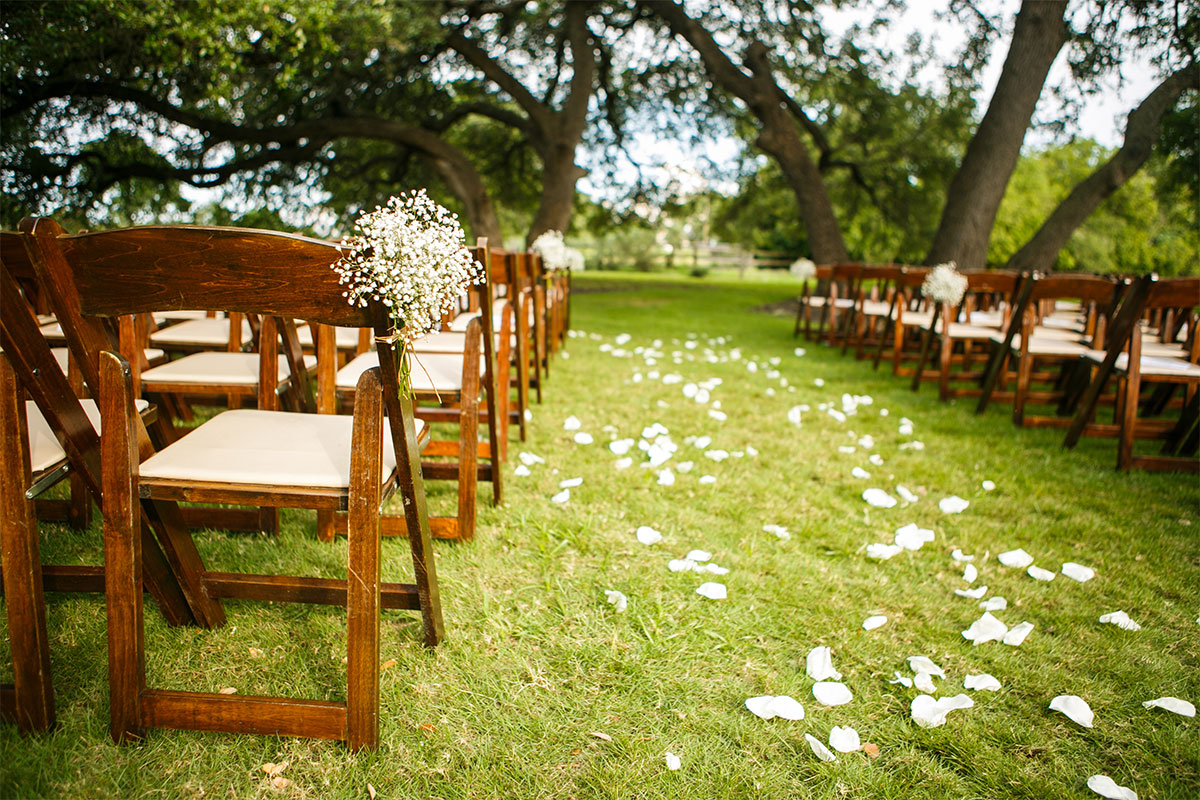 outdoor wedding venue with wooden chairs and petals down the aisle.