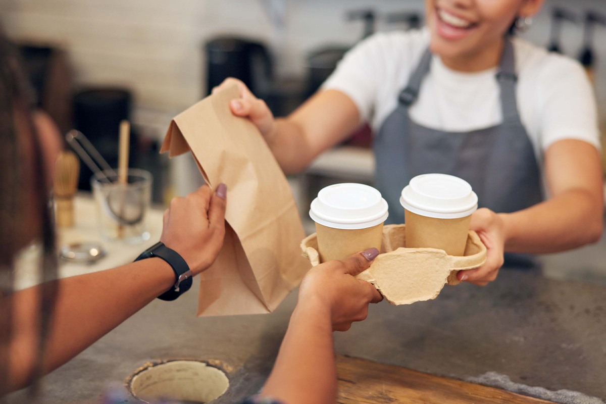 barista handing drinks and paper bag to customer in coffee shop